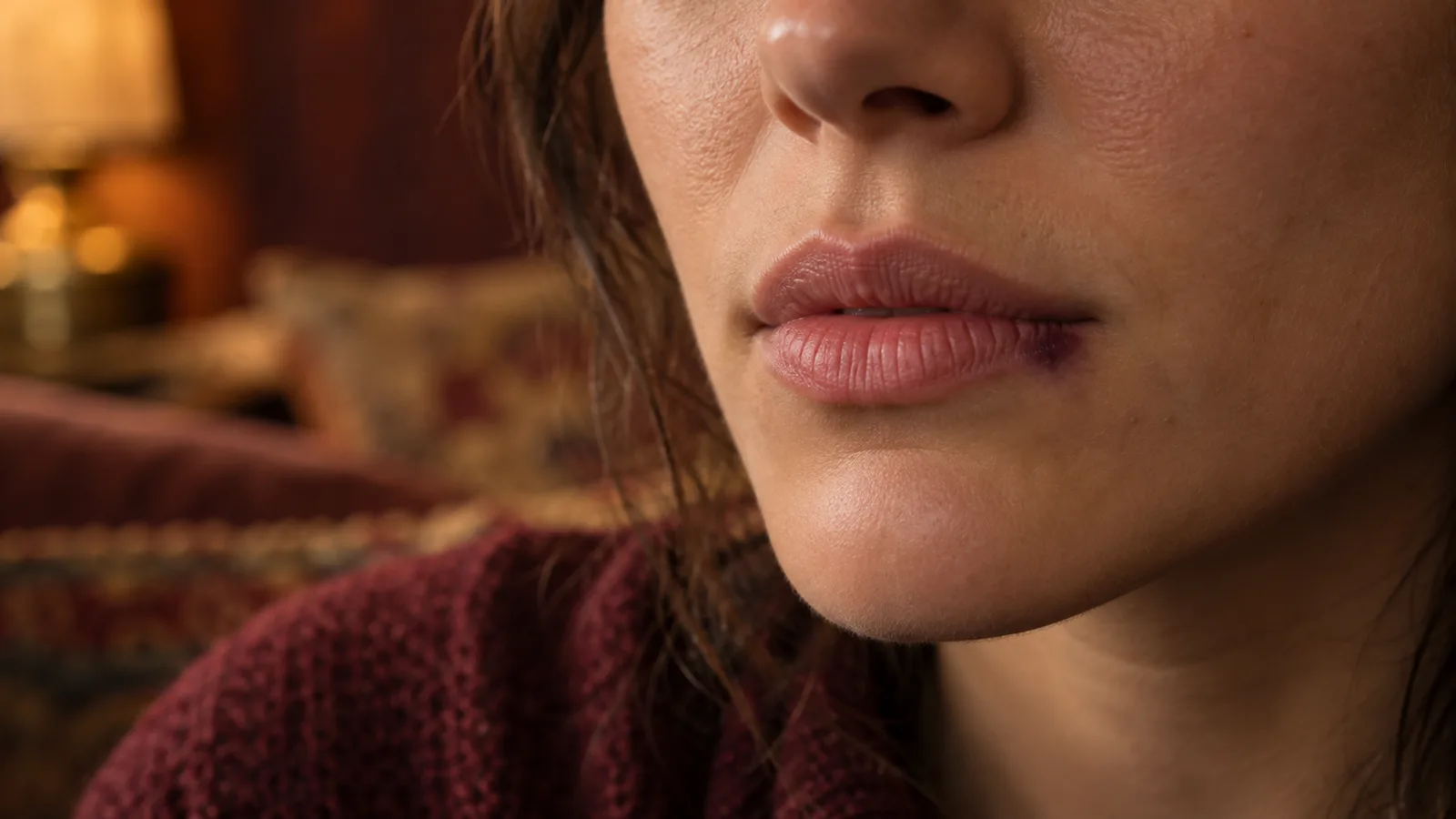 Close-up of a woman's lower face with a small faint bruise at the corner of her lip.